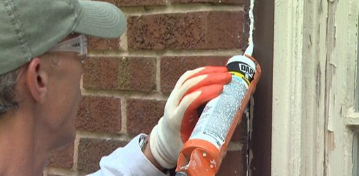 A person using a caulk to seal a crack in a brick wall